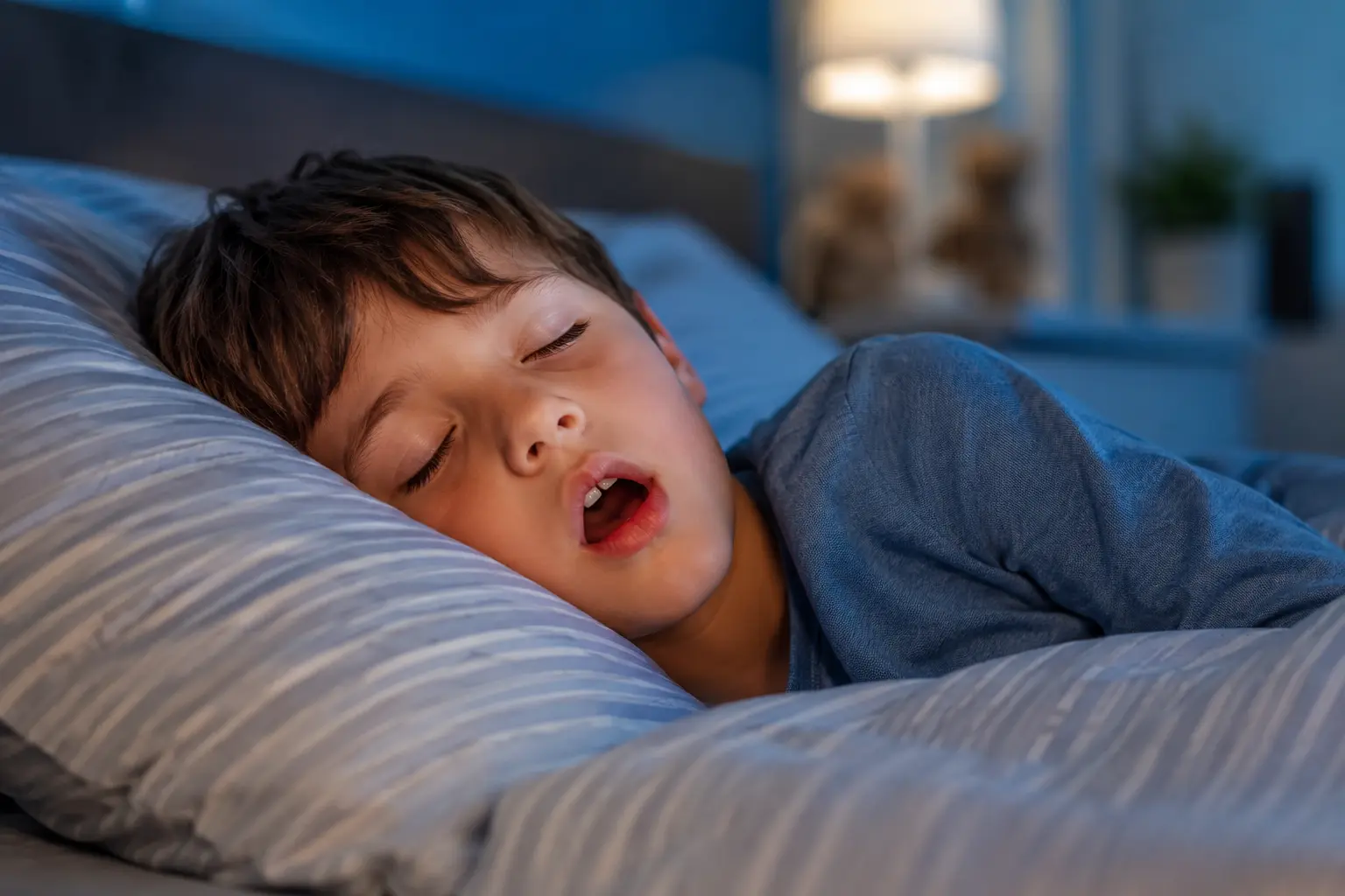 Child sleeping with mouth open in bed, highlighting concerns about mouth breathing in kids and its connection to sleep, focus, and airway development.
